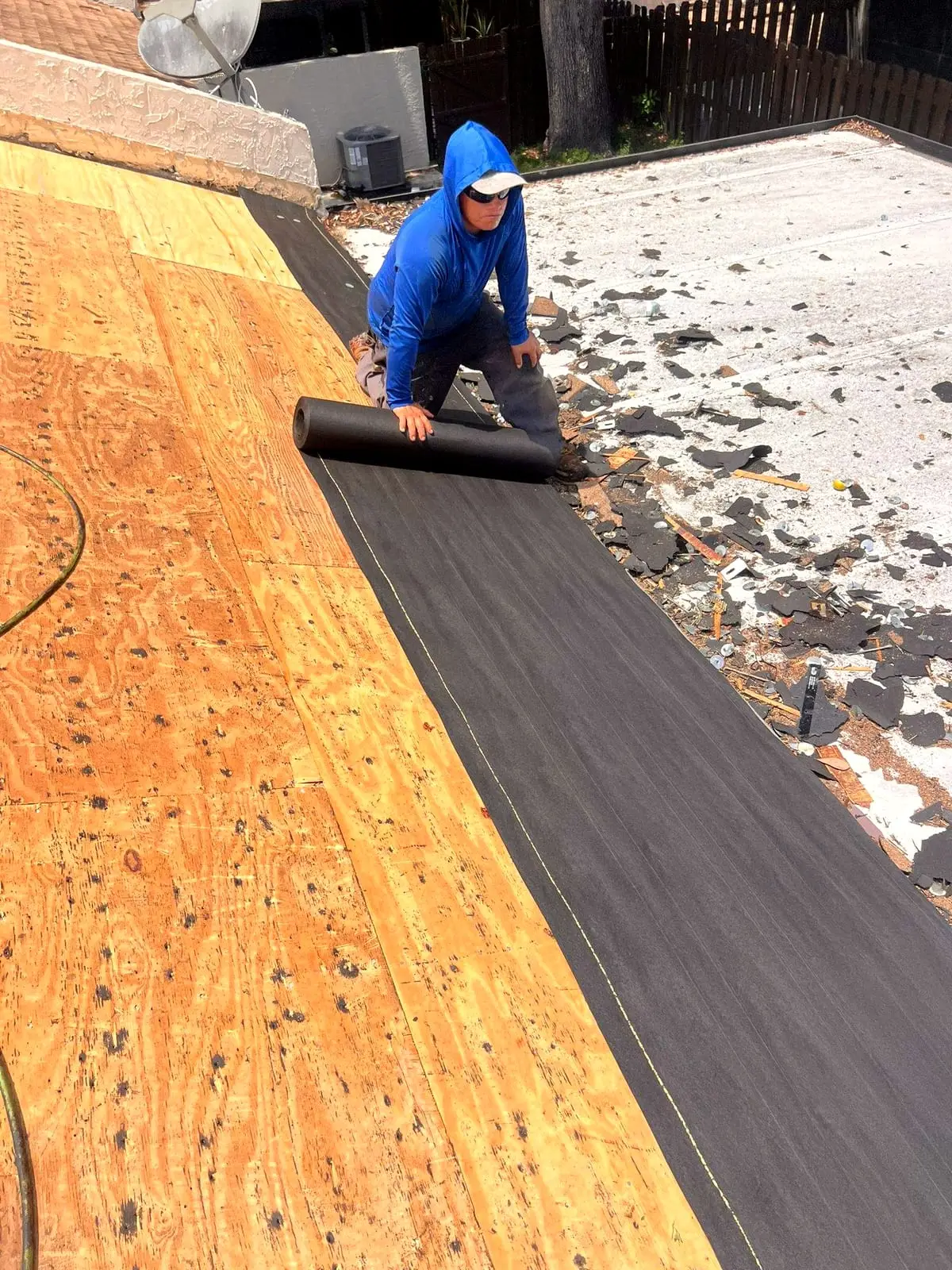 A roofer rolling out underlayment over the plywood roof deck