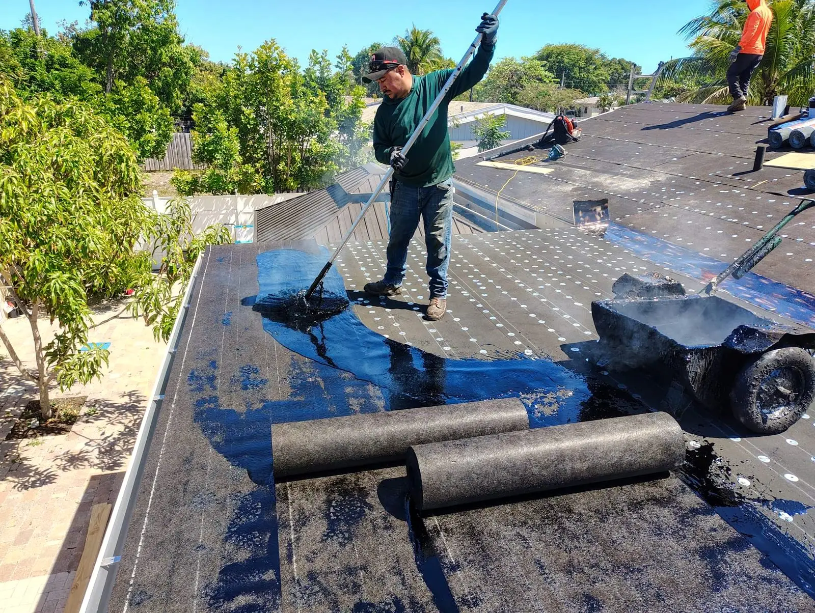 A roofer working on a flat roof, with rolls of roofing felt laid out