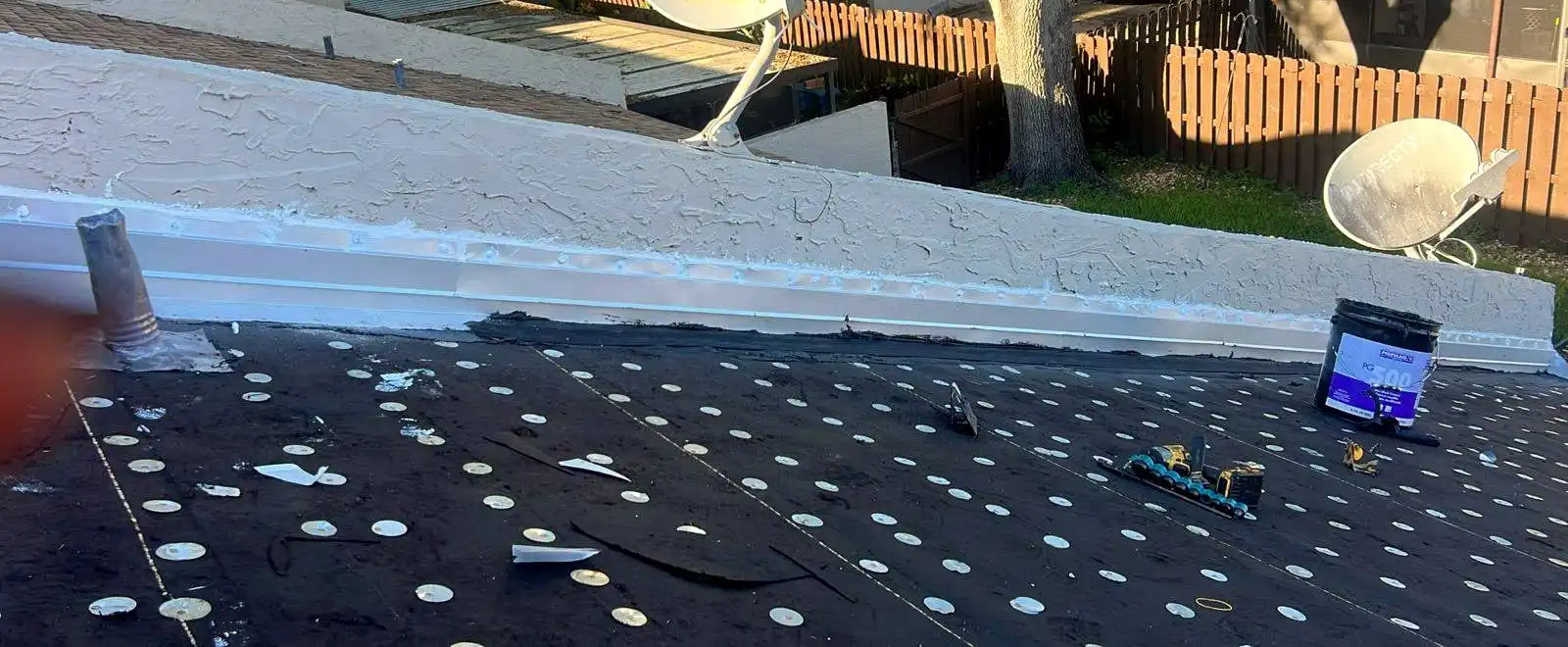 A low-slope roof dried in against a stucco wall, with metal flashing along the joint