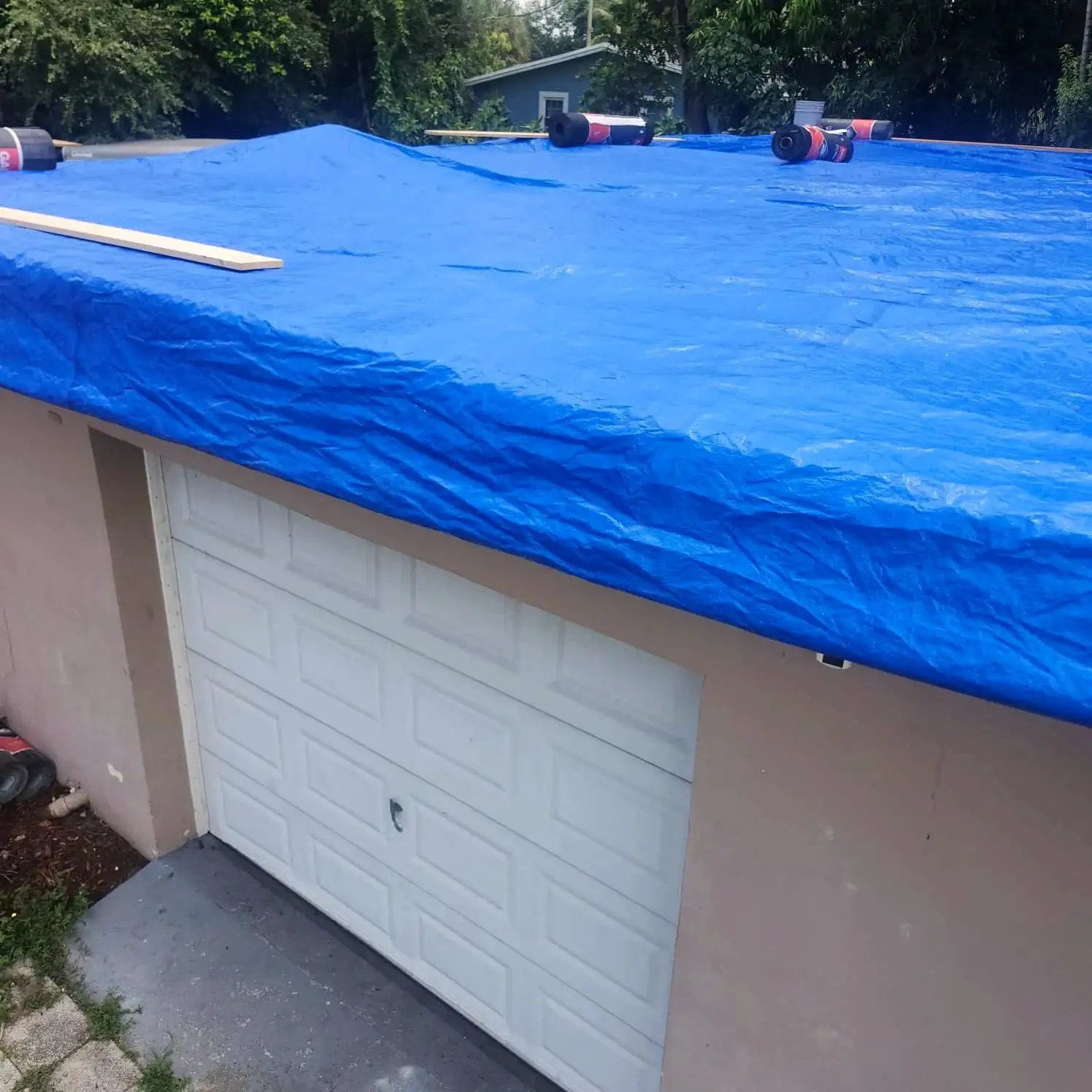 A blue tarp secured over a roof above a garage