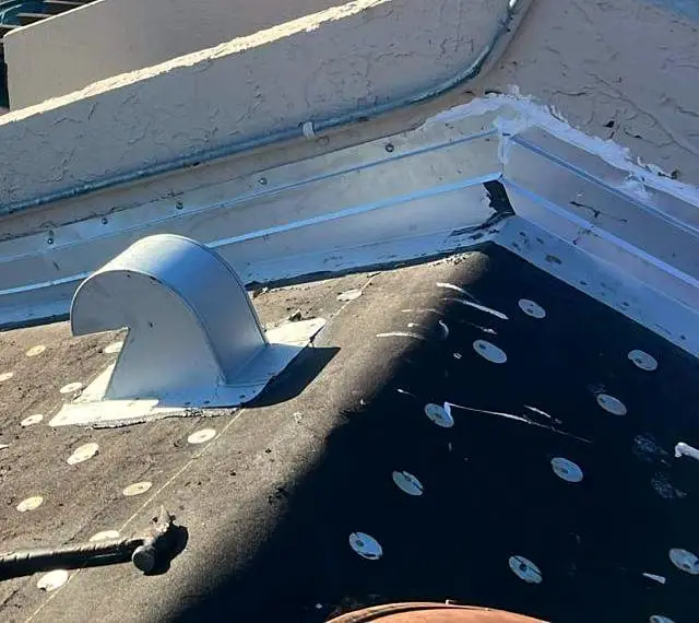 Metal flashing where a roof meets a wall, with a roof vent set into the dried-in deck